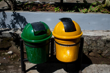 a pair of green and yellow trash cans, with black iron pillars, plant background, visible in the daytime