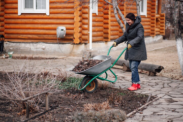 Woman worker in field clothes applying mulching procedure, gathering old dried leaves, bark in...