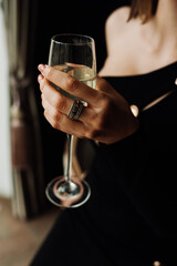 female hand with nude manicure in a black dress with a neckline hold a cold wet glass of white wine, vertical, selected focus