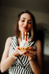 young woman smiles and prepares to blow out the candles on a small cake. the woman's face is unrecognizable. vertical birthday content, selective focus