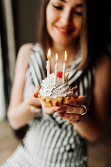 young woman smiles and prepares to blow out the candles on a small cake. the woman's face is unrecognizable. vertical birthday content, selective focus