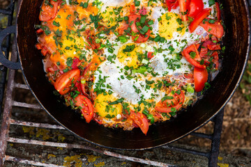 Eggs prepared with vegetables on a frying pan on the fire in the forest. Cooking scrambled eggs over an open fire. Breakfast in nature. Tourist food.