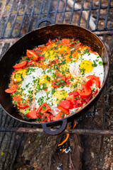 Eggs prepared with vegetables on a frying pan on the fire in the forest. Cooking scrambled eggs over an open fire. Breakfast in nature. Tourist food.