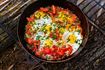 Eggs prepared with vegetables on a frying pan on the fire in the forest. Cooking scrambled eggs over an open fire. Breakfast in nature. Tourist food.