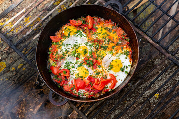Eggs prepared with vegetables on a frying pan on the fire in the forest. Cooking scrambled eggs over an open fire. Breakfast in nature. Tourist food.