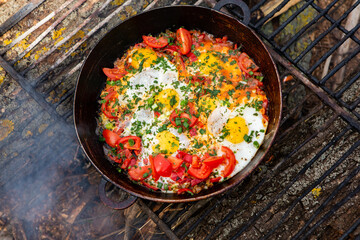 Eggs prepared with vegetables on a frying pan on the fire in the forest. Cooking scrambled eggs over an open fire. Breakfast in nature. Tourist food.