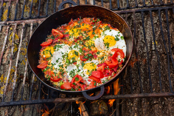 Eggs prepared with vegetables on a frying pan on the fire in the forest. Cooking scrambled eggs over an open fire. Breakfast in nature. Tourist food.