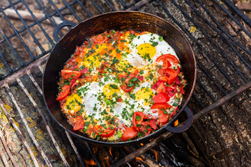 Eggs prepared with vegetables on a frying pan on the fire in the forest. Cooking scrambled eggs over an open fire. Breakfast in nature. Tourist food.