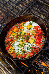 Eggs prepared with vegetables on a frying pan on the fire in the forest. Cooking scrambled eggs over an open fire. Breakfast in nature. Tourist food.