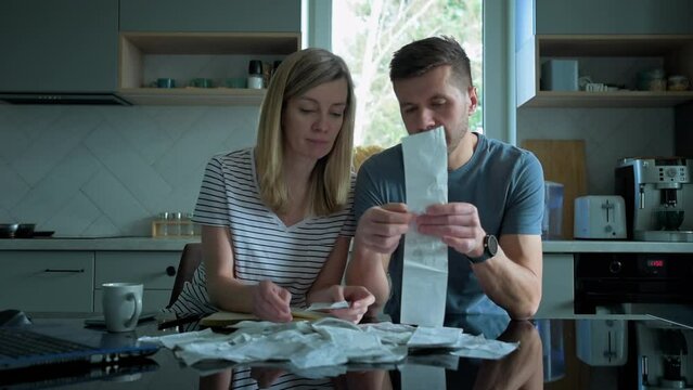 Man and woman checking payment bills in the kitchen at home. Planning family budget. Couple calculate bills and have stress