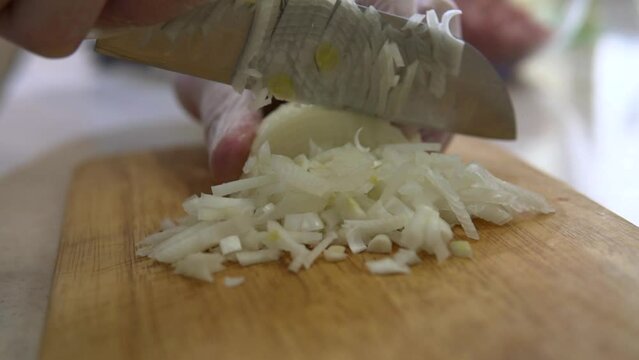 Cutting white onion. Chef uses a kitchen knife to chop the vegetable on a wooden cutting board. Making healthy food ingredient for cooking. 