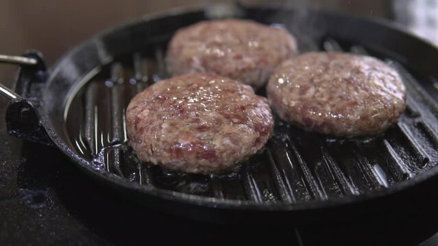 Cooking beefstakes patties for burger. Roasting fat meat cutlet for hamburger on a metal grill frying pan at restaurant kitchen. American unhealthy fastfood making.