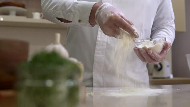 Flour powder falling from hand. Chef pouring and sifting wheat meal for cooking preparation on a kitchen. 