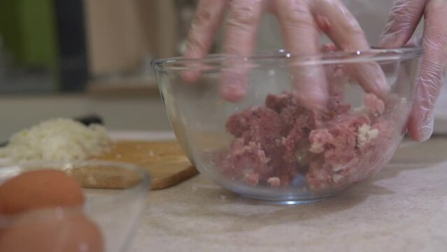 Beef ground meat making. Chef mixing fresh, raw minced meat and onion in a glass bowl for burgers, cutlets and beefstakes. Kitchen preparation of semifinished product.
