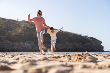 Happy mother and daughter jumping on sand at beach