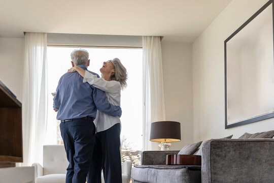 Happy senior couple dancing in living room at home - Powered by Adobe