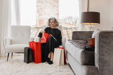 Smiling woman sitting on armchair with sopping bags at boutique hotel