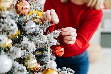 Woman decorating Christmas tree with bauble at home