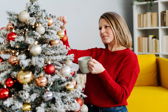 Woman with coffee cup looking at ornament on Christmas tree