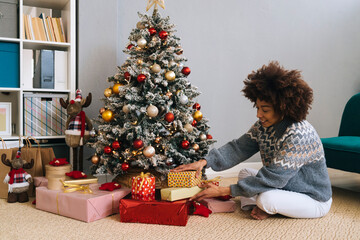 Smiling woman arranging gifts by Christmas tree at home