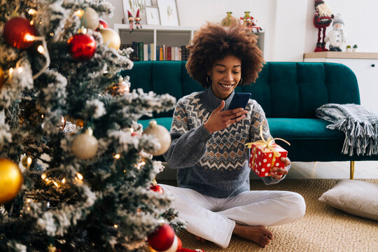 Smiling young woman photographing Christmas present through mobile phone at home