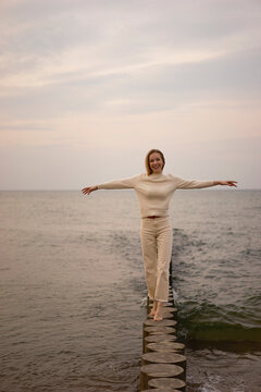 Happy woman with arms outstretched walking on wooden post at beach