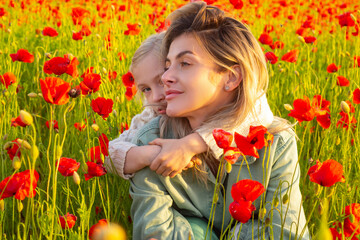 Mother and daughter hugging on spring meadow. Beautiful child girl with young mother are wearing casual clothes in field of poppy flowers. Family on spring poppy field.
