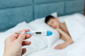 A woman's hand holds an electronic thermometer on a white-gray wooden background. High quality photo