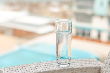 A glass of clean water in the open air. Glass glass with water on the background of the pool. Soft focus.