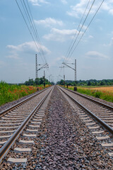 Obraz premium Cover page with railway for trains in beautiful farm landscape with wheat yellow field and poppy red flowers at warm sunset colors in summer, at sunny day and blue sky.