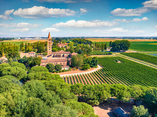 Fresh green scene of Pomposa Abbey tower among vineyards. Aerial summer view from flying drone of Italian countryside, Province of Ferrara, Italy. Country tourism and travel concept image.