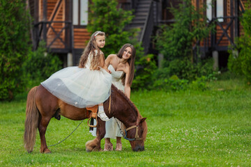 mother rides her daughter on a pony on a green lawn