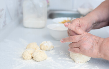 Senior woman hands kneading dough on a white kitchen table with blurred grated apple and sugar on background. Selective focus. Process of making pies with apple filling. Cooking at home concept. 