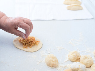 Senior woman hands put the apple filling on the dough for pies on a white kitchen table. Selective focus. Process of making pies with apple filling. Cooking at home concept. Tradition home-made food