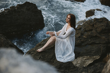 pretty woman with wet hair in a white dress on the coast sits on the rocks