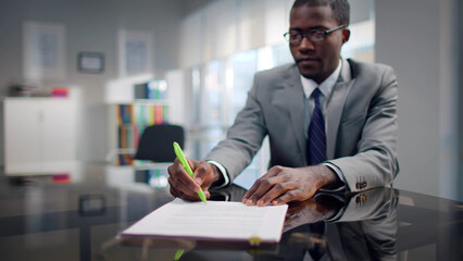 African-American investor sign contract sitting at desk in modern workplace with blurred background