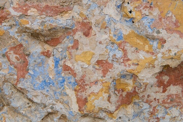 Detail of the colorful, textured exterior wall of an old, painted, peeling stucco building revealing many layers of different colored paint applied over the years.