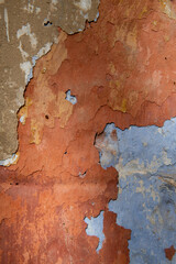 Detail of the colorful, textured exterior wall of an old, painted, peeling stucco building revealing many layers of different colored paint applied over the years.