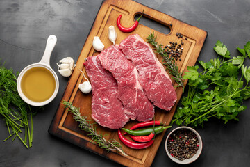 Fresh raw beef meat on cutting board on dark background with ingredients for cooking top view