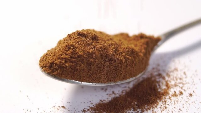 Instant roasted chicory root powder with cereal additives to replace traditional coffee. Full spoon of organic herbal substitute on white background. Falling particles in slow motion. Macro. Rotation