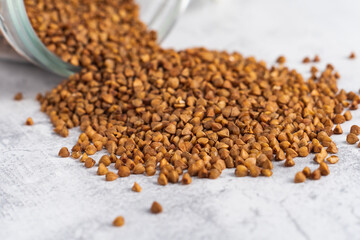 Close-up buckwheat grain poured from glass jar on gray table. Selective focus