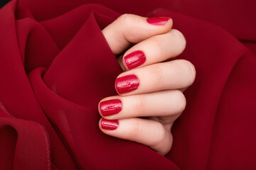 Female hand with red nail design. Glitter red nail polish manicure. Female model hand on red fabric background
