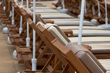Wooden brown chairs for sunbathing stand in a row by the pool. Tourists who come to rest, after...
