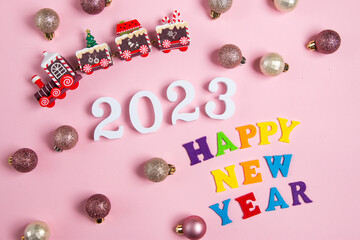 White numbers in the shape of 2023 and New Year's baubles on a pink background. Flat lay with place for text.