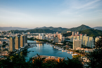 Fototapeta na wymiar Panoramic view of Sanya city and bay. Skyscrapers against the backdrop of mountains among green trees. Buildings are located on the beach.