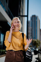 Fototapeta premium Happy girl walking on the street using the phone. Beautiful blonde girl talking to the smartphone