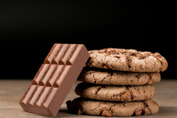 brown chocolate chip cookie large poan.  On a black background. Chocolate chip cookies with brown chocolate chips are placed on a wooden table.