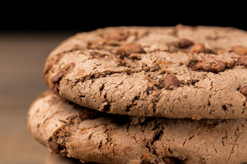 brown chocolate chip cookie large poan.  On a black background. Chocolate chip cookies with brown chocolate chips are placed on a wooden table.