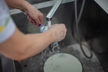 Woman washes dishes under stream of water. Kitchen details. Dishwasher cleans spoon in sink.