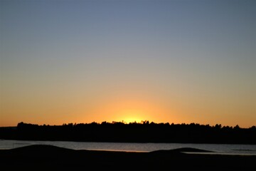 Gold sunset after dark forest and lake